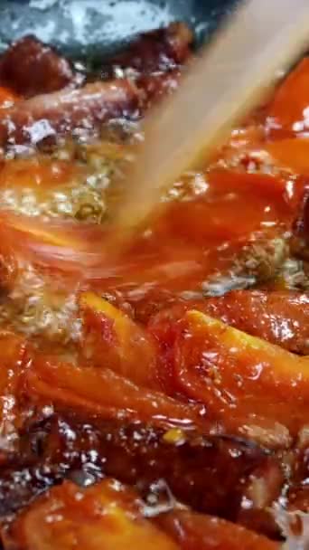 Deliziose salsicce da caccia grasse, tagliate a pezzi e tagliate a fette di pomodoro vengono fritte in padella in olio vegetale. Fast food nutriente. Cucina casalinga. Video verticale. Primo piano. — Video Stock