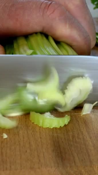 Les mains du chef hachent la tige de céleri en petites tranches avec un couteau de cuisine sur une planche de cuisine en bois pour salade de légumes. céleri frais et sain pour manger et cuisiner. Vidéo verticale. Gros plan. — Video