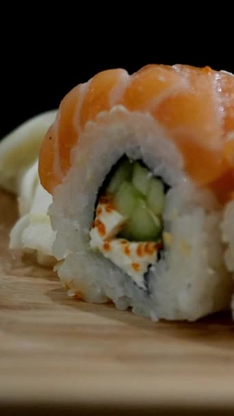 Japon yemeği. Ahşap tahtadan somon balıklı suşi rulosunu al ve kaldır. Seçici odaklanma. Dikey video. Yakın plan.. — Stok video