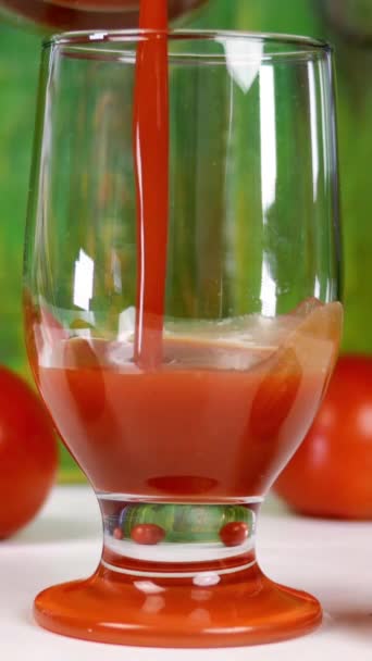 Giet vers tomatensap in leeg doorzichtig glas, naast verse rijpe natuurlijke tomaten. Gezonde vegetarische drank met veel vitaminen. Verticale video. Selectieve focus. — Stockvideo