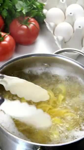 Kock matlagning pasta i kastrull. Tillagning italiensk tagliatelle i hemkök. Koka med tång blanda pasta i kastrull. Svamp, ägg, tomater. Vertikal video. — Stockvideo