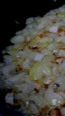 İnce doğranmış soğanlar haşlanmış sebze ya da zeytinyağında tavada kızartılır ve mutfak spatulasıyla iyice karıştırılır. Ev mutfağı. Dikey video. Dolly vurdu. Yakın plan..