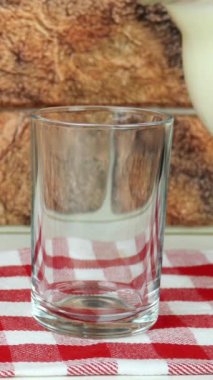 Taze doğal süt, sürahiden duvara dayanan sürahiye, kafes peçetesine dökülüyor. İçme bardağını sütle dolduruyorum. Sağlıklı süt ürünleri gıda konsepti. Dikey video.