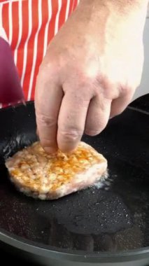 Şef mutfak masasındaki evcil mutfakta hamburger için tavuk pirzolası hazırlıyor. Sıcak tavaya kıyma, yağ ve biberiye filizleriyle garnitür koyuyor. Dikey video.