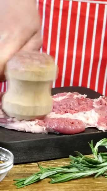 Chef bate las rebanadas frescas crudas de carne de cerdo con martillo de cocina antes de cocinar en la tabla de cortar. Preparación rompiendo chuletas de carne de cerdo. Espolvorear con especias. Vídeo vertical. Dolly disparó. — Vídeo de stock