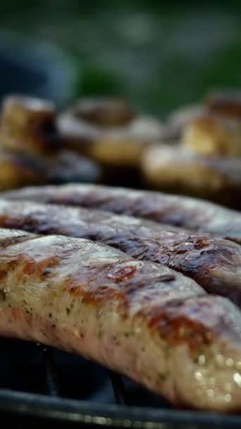 Жареные жирные баварские сосиски, приготовленные на гриле или гриле. С грибами. Вертикальное видео. Крупный план. — стоковое видео