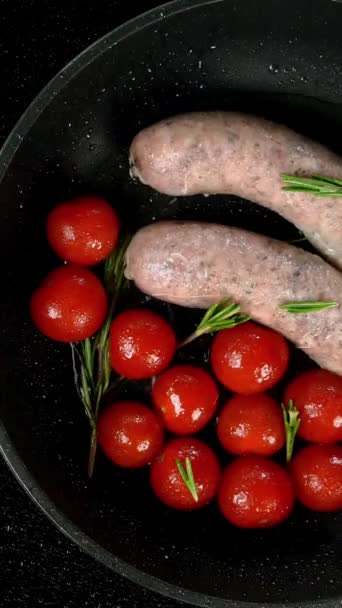 Saucisses bavaroises blanches grasses avec tomate et brin de romarin frit dans une poêle sur une cuisinière électrique. Petit déjeuner anglais ou allemand, européen ou américain. Vue de dessus. Vidéo verticale. — Video