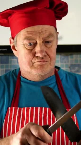 Senior vuxen kock kaukasisk etnicitet i kockar hatt vässar kniv på kniv på hushållsköket. — Stockvideo