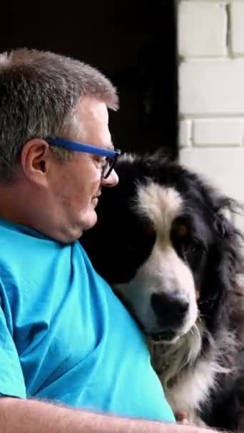 Senior vuxen man klappa och krama sin Bernese Mountain Dog, medan sitter på verandan av hus. Begreppet kärlek och vänskap för husdjur. — Stockvideo