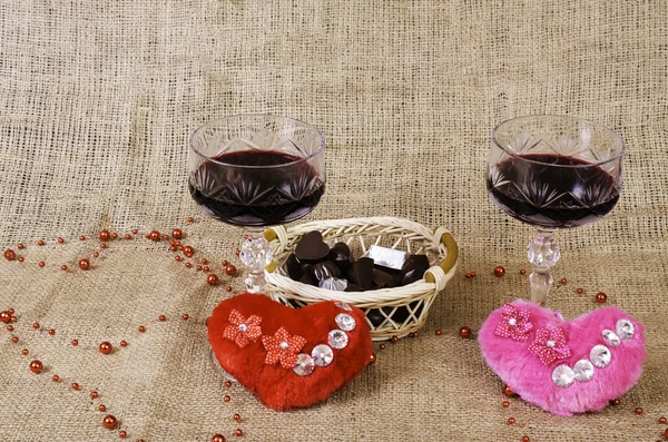 Glasses of wine, two hearts and a basket with chocolate. — Stock Photo, Image