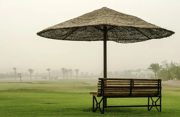 Banc dans le désert sous un parapluie du soleil . — Photo