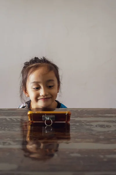 Önünde cep telefonuyla masada oturan küçük bir kızın portresi. Cep telefonundan video izliyordum..