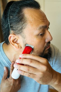 Asyalı adam elektrikli tıraş makinesiyle sakal tıraş ediyor..