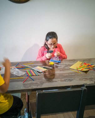 Genç bir kız yapıştırıcı tabancasıyla renkli plastik çubuklar yapıyor. Geometrik figürler oluşturmak ve evde matematik öğrenmek eğlenceli.