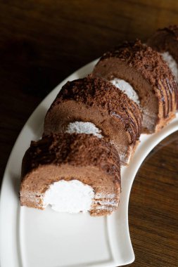 Beyaz bir tabakta taze kremalı çikolata rulosu ve ahşap arka plan.