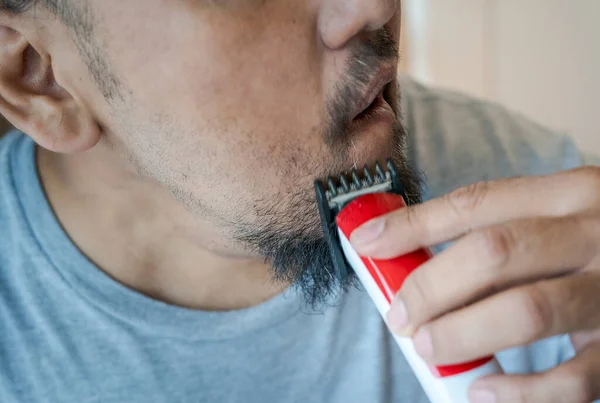 Asian man shaving beard with electric razor machine.