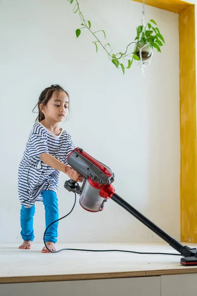 Elektrikli süpürgeyle ahşap zemini temizleyen tatlı küçük kız.