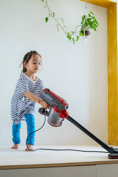 Cute little girl cleaning wooden floor with vacuum cleaner