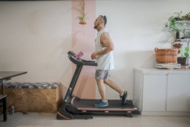 Evde koşu bandında koşan sakallı olgun bir adamın profil fotoğrafı.