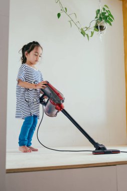 Elektrikli süpürgeyle ahşap zemini temizleyen tatlı küçük kız.