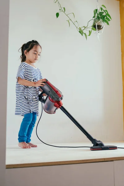 Elektrikli süpürgeyle ahşap zemini temizleyen tatlı küçük kız.