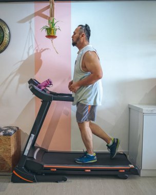 Evde koşu bandında koşan sakallı olgun bir adamın profil fotoğrafı.