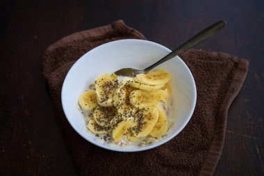 Yakın plan mısır gevreği kasesi ve arka planda Chia tohumları serpiştirilmiş dilimlenmiş muz..