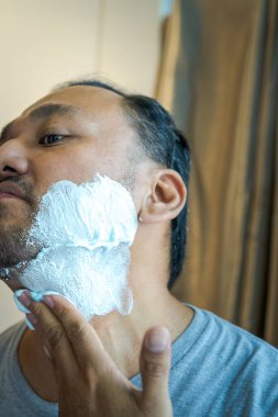 Asyalı bir adamın yüzüne tıraş kremi sürüyorum..