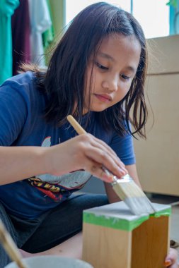 Genç bir kız kutuları beyaza boyuyor. Güncelleme, geri dönüşüm ve ev yenileme projesi.