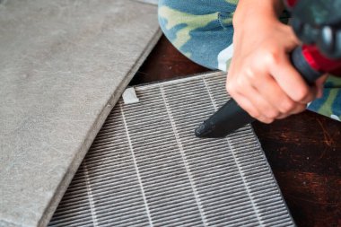 Genç bir çocuk süpürgeyle hava filtresi örtüsünü temizliyor..