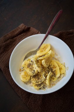 Yakın plan mısır gevreği kasesi ve arka planda Chia tohumları serpiştirilmiş dilimlenmiş muz..