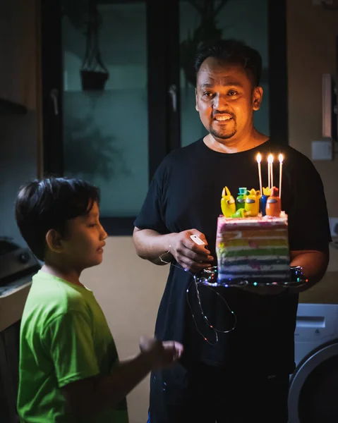 爸爸在家里拿着一个蛋糕 上面点着蜡烛 送给孩子们过生日的惊喜 — 图库照片