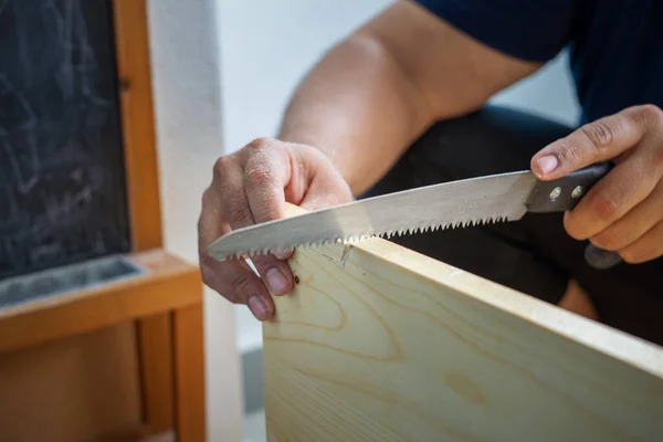 Carpenter hand with saw cutting wooden boards