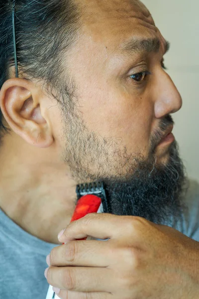 Asian man shaving beard with electric razor machine.