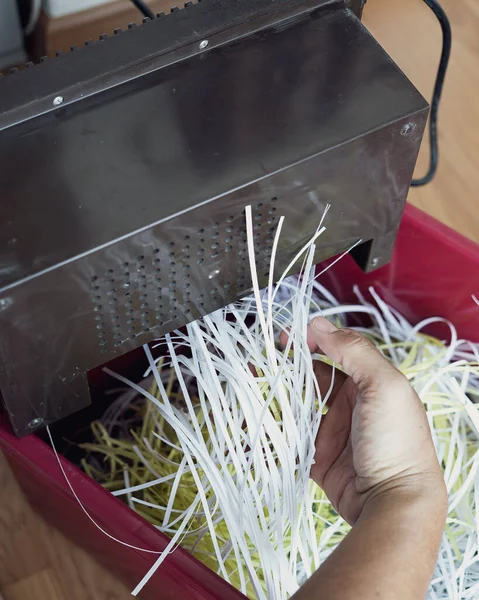 Shredding paper coming out from the machine with hand pulling.