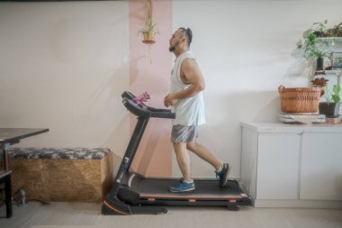 Evde koşu bandında koşan sakallı olgun bir adamın profil fotoğrafı.