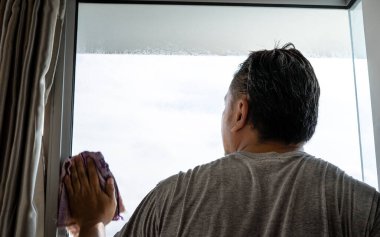 Ev temizliği kavramı. Pencerede bir adam var ve bir bez parçasıyla siliyor. Arkadan görünüm.