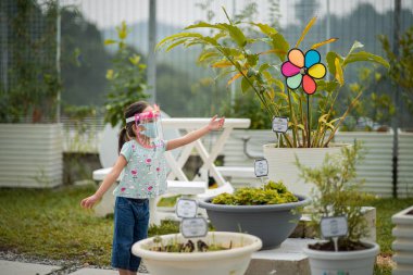 Kuala Lumpur, Malezya - 10 Temmuz 2021: Coronavirus salgını sırasında bitki bahçesinde yürüyen sevimli bir anaokulu çocuğunun yüz maskesi taktığı bulanık fotoğraf.