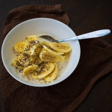 Yakın plan mısır gevreği kasesi ve arka planda Chia tohumları serpiştirilmiş dilimlenmiş muz..