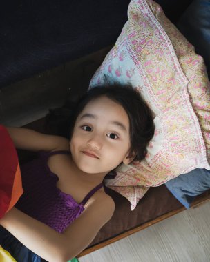 Oturma odasında gökkuşağı elbisesiyle uzun bir sandalyede uzanan sevimli küçük bir kızın bulanık fotoğrafı. Üst görünüm.