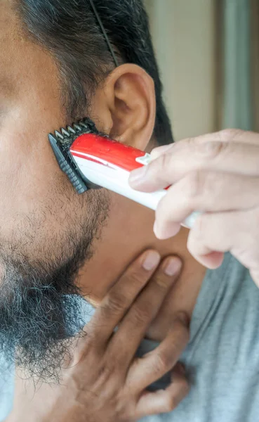 Man shaving beard with electric razor machine. Close-up.