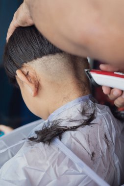 Genç bir çocuk evde elektronik traş makinesi kullanarak babasından saç tıraşı oluyor. Yandan görüntüle.