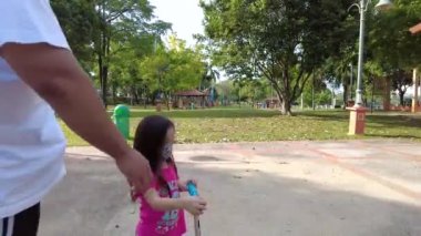 Bangi, Malezya - Mart 2021 Baba güneş gözlüğü takıyor kızını parkta scooter 'a bindiriyordu. Görüntü düşük ışıktan dolayı gürültü içerebilir.