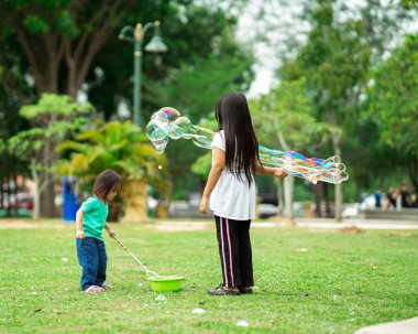Parkta sabun köpüğüyle oynayan sevimli aktif Asyalı kız kardeşler.