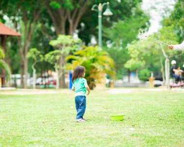 Parkta sabun köpüğüyle oynayan sevimli aktif Asyalı kız.