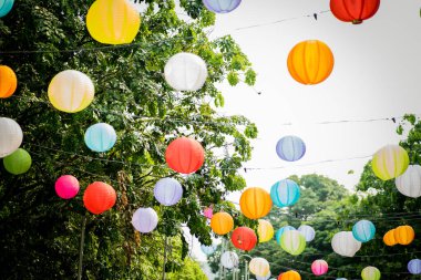 Arkaplanda ağaçlar ve gökyüzü asılı renkli kağıt fener..