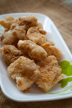 Malezya usulü dövülmüş ve kızartılmış dory balığı küpleri. Kahverengi arka planda uzun bir tabakta servis edilmiş.