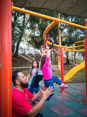 Babasıyla maymun parmaklıklarındaki çocuk. Spor salonunda takılan küçük bir kız. Çocuklar için sağlıklı bir açık hava aktivitesi. Küçük çocuklar için spor.