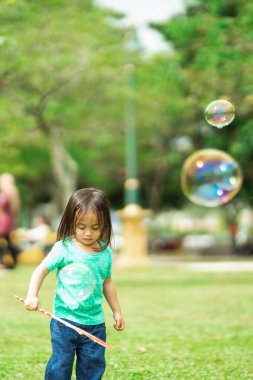 Parkta sabun köpüğüyle oynayan sevimli aktif Asyalı kız.