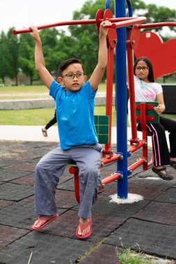 Erkek ve kız kardeş parkta egzersiz makineleriyle çalışıyor.
